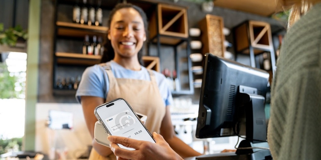 Eine Kundin bezahlt an einer Café-Theke kontaktlos mit dem Smartphone / MLP