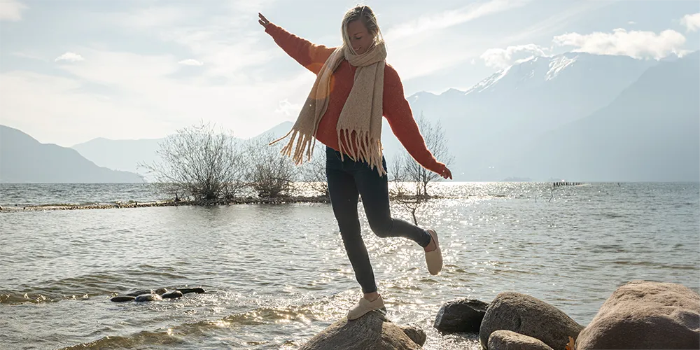 Eine Frau balanciert auf einem Stein im Wasser.