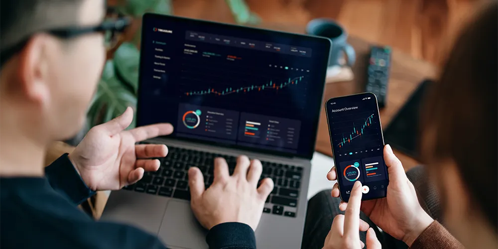 Zwei Personen schauen auf Handy und Laptop und vergleichen Rendite und Risiko ihrer Anleihen-ETFs.