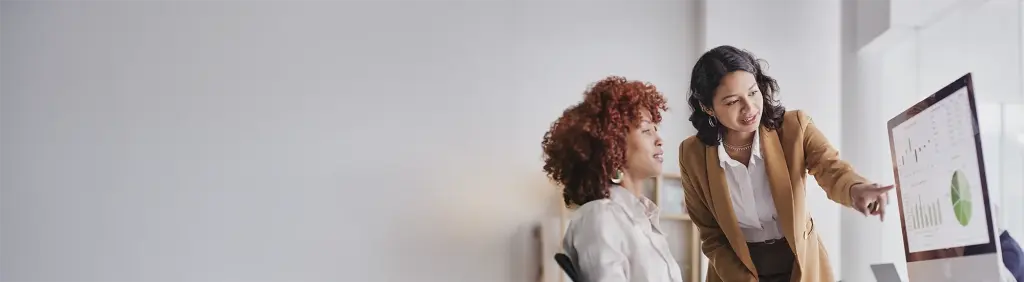 Eine Frau zeigt einer anderen Frau auf einem Bildschirm deren Dividendenausschüttung.