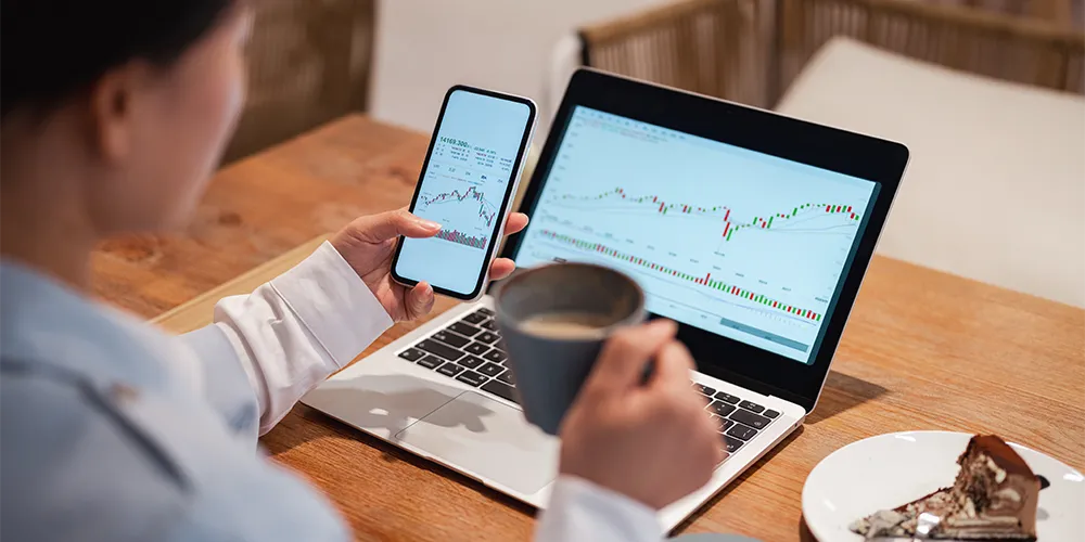 Eine Person betrachtet die Kursentwicklungen ihrer festverzinslichen Wertpapiere auf dem Laptop und Smartphone.