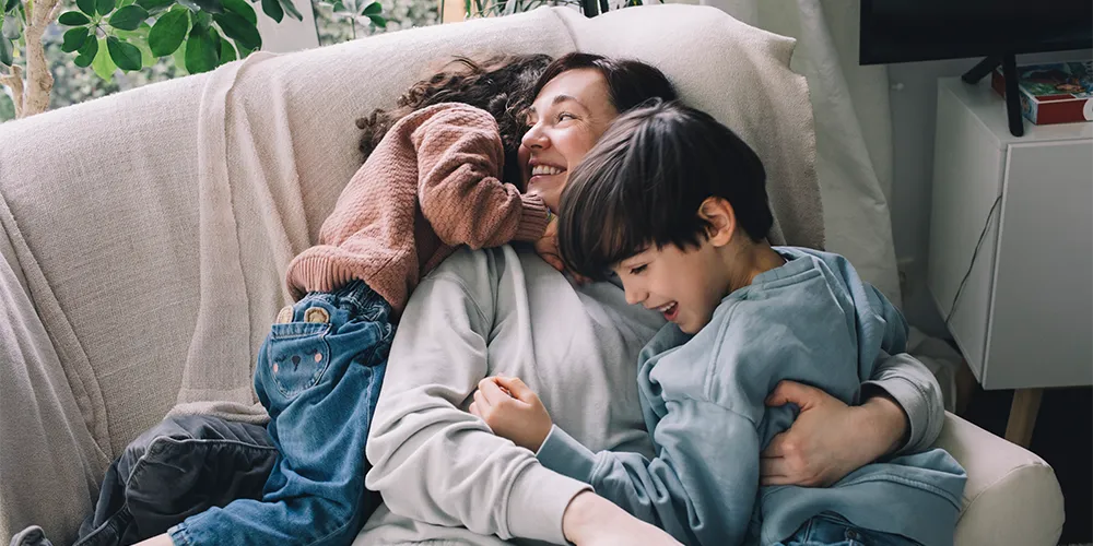 Eine Mutter spielt unbeschwert mit ihren Kindern, die sie über ein Junior Depot finanziell abgesichert hat.