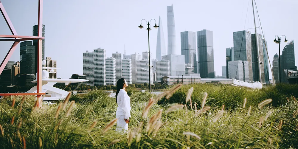Eine junge Frau steht vor der Skyline einer Stadt auf einer Wiese.