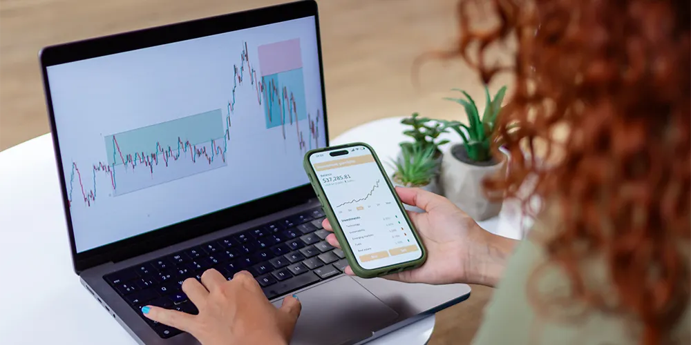 Eine Person sieht sich auf dem Laptop und Smartphone die Kursentwicklungen ihres Wertpapiersparplans an.