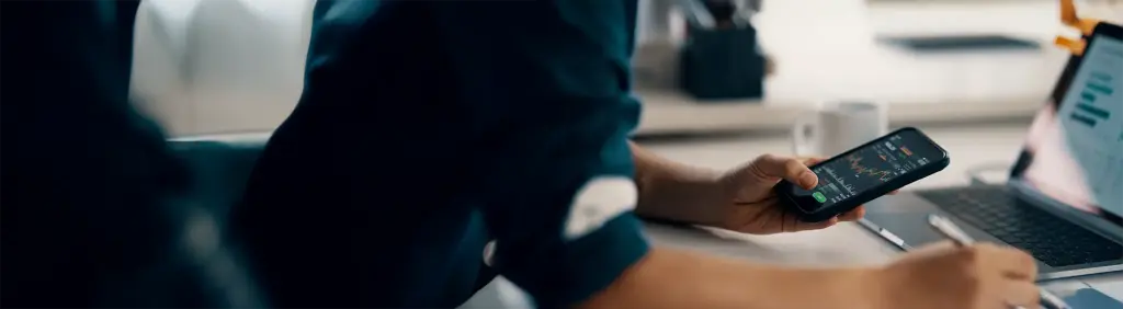 Eine Person schaut sich amSmartphone und Laptop die Entwicklung ihres Wertpapiersparplans an