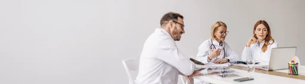 Mehrere Ärztinnen und Ärzte diskutieren an einem Tisch über das Qualitätsmanagement in ihrer Arztpraxis.