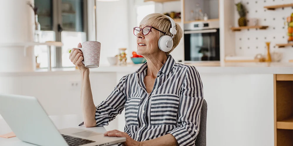 Ältere Frau am Schreibtisch mit Kaffetasse in der Hand