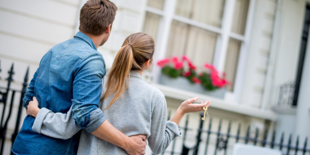 Paar bewundert Arm in Arm ein Haus. Die Frau hält einen Schlüssel in der Hand.