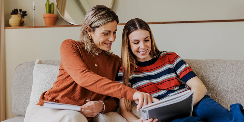Mutter und Tochter sitzen auf dem Sofa und besprechen an einem Tablet die Kosten des Studiums.